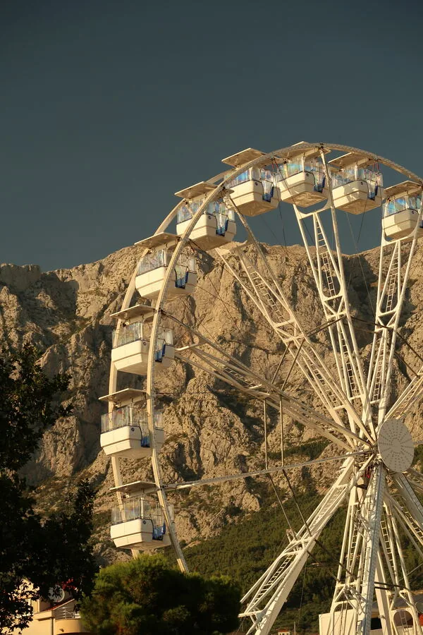 A white ferris wheel standing against a limestone cliff at golden hour.