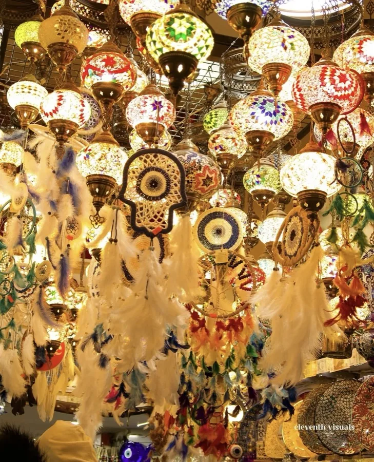 Colourful mosaic lamps and feather dreamcatchers hanging close together in a bazaar shop.