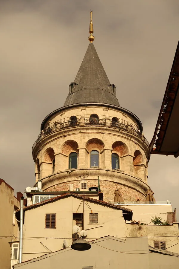 The Galata Tower in Istanbul, its stone cone and arched windows warm against a pale evening sky.