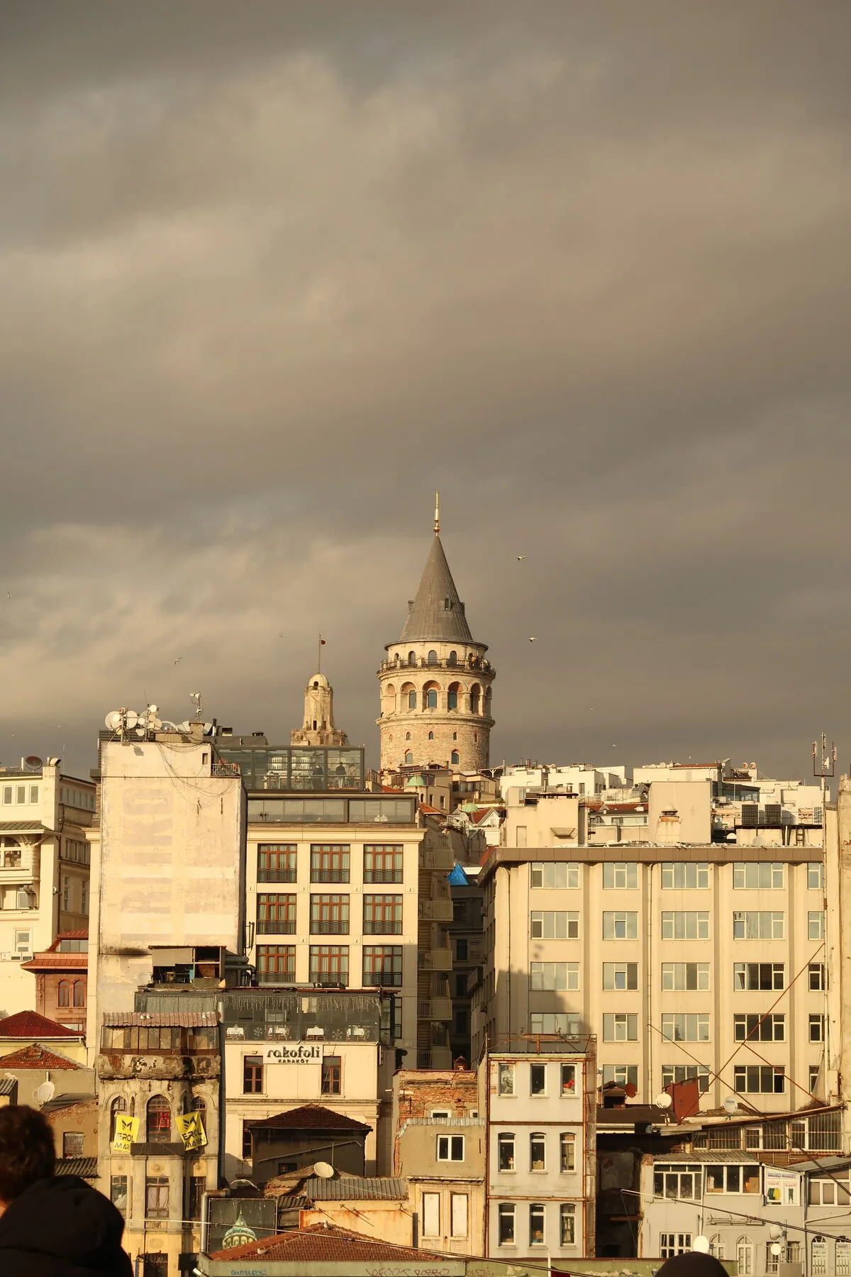 Galata Tower rising over a dense stack of Istanbul rooftops under a heavy sky.