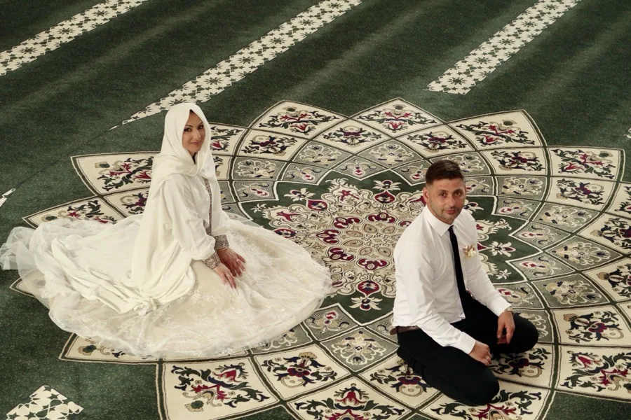 The bride and groom kneeling on an ornate green carpet, looking up at the camera.