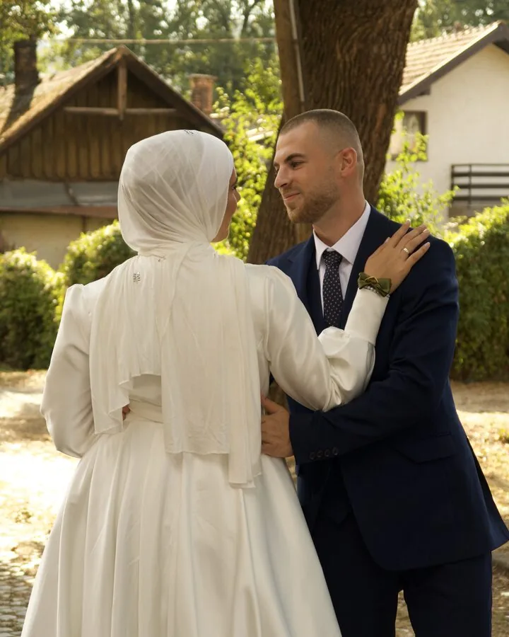 The bride seen from behind, her hand on the groom's shoulder, the two of them talking under a tree.