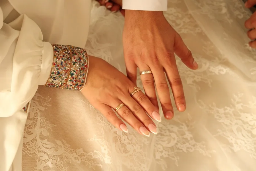 Close frame of the couple's hands with wedding rings, resting on white lace.